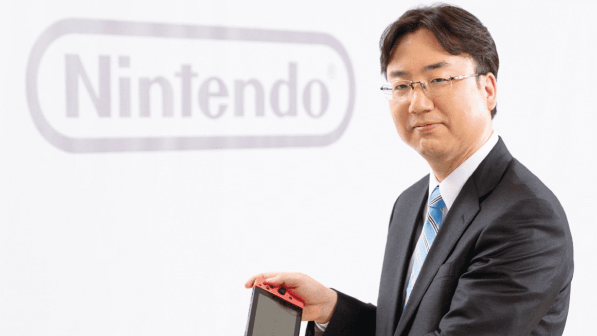 Nintendo President Shuntaro Furukawa holding a Switch in front of the Nintendo logo.
