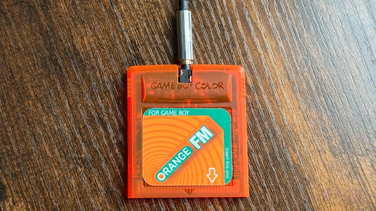 A headphone cable sticking out of an Orange FM Game Boy cartridge 