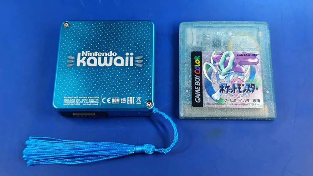 Photo of a small, shiny blue square bit of hardware labelled Kawaii, next to a blue Pokémon Gameboy cartridge