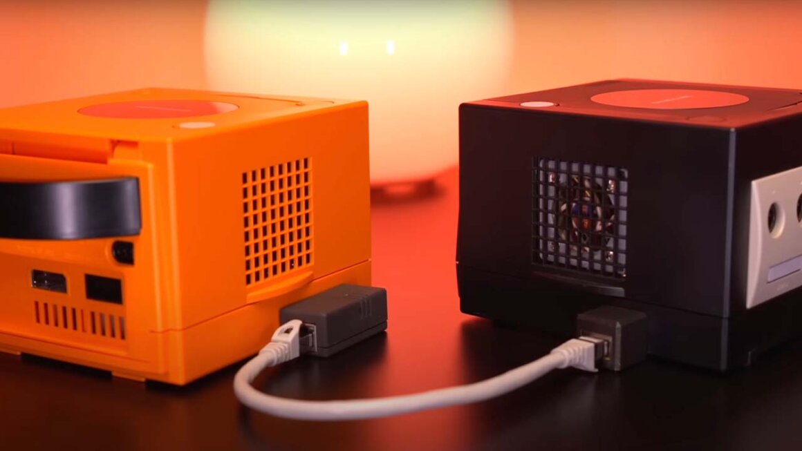 Two GameCubes (one orange, one black) connected in LAN mode via two connectors