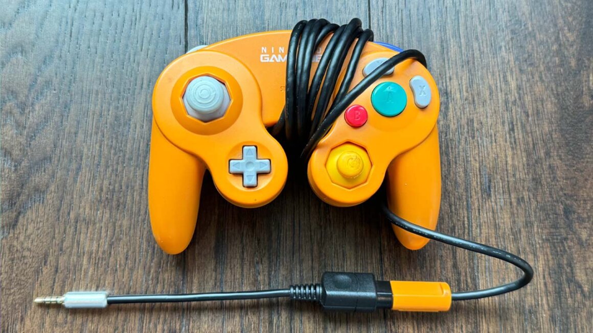 An orange Gamecube controller with a headphone jack adapter on the end of the wire