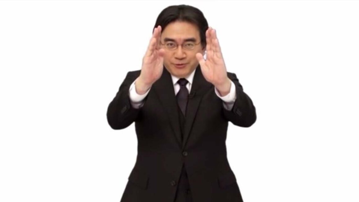 Satoru Iwata holding his hands up and looking at the screen